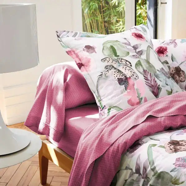 Oreiller floral rose avec une impression botanique de style aquarelle sur fond blanc, mettant en vedette des roses pastel doux et des verts atténués.