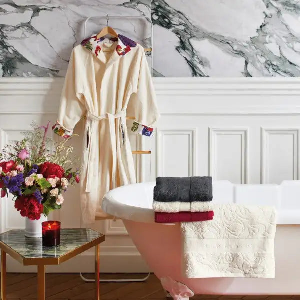 Robe de couleur crème avec broderie florale sur le col et les poignets, suspendue proprement sur un porte-peignoir blanc.